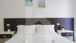 A modern hotel room with a large bed, white linens, two bedside tables with plants, and artwork on the walls. - Homiday - Felicioni Alba Adriatica, Trilocale al Piano Terra (Alba Adriatica)