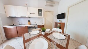 A modern kitchen with white cabinets, a built-in oven, and a dining area with a wooden table set for four. - Homiday - Felicioni Alba Adriatica, Trilocale al Piano Terra (Alba Adriatica)
