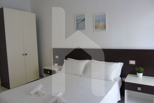 A hotel room with a bed, a wardrobe, a nightstand, a bedside table, and two wall-mounted pictures.