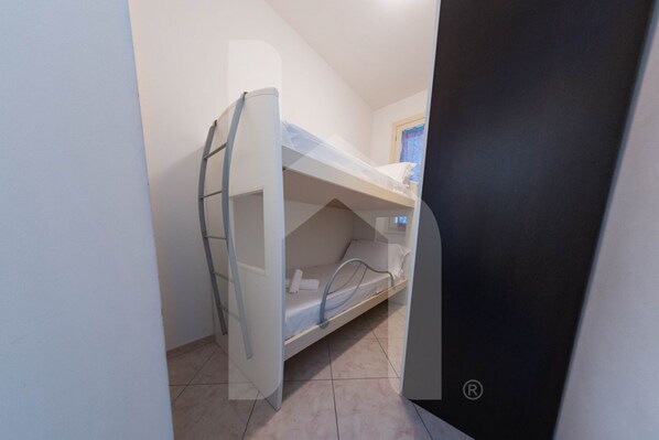 Un lit superposé avec une échelle, une fenêtre avec des rideaux bleus et un petit bureau avec une chaise.