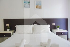 A modern hotel room with a large bed, white linens, two bedside tables with plants, and artwork on the walls.
