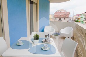 En balkon med et bord dækket til to, hvide stole og krukker med planter.