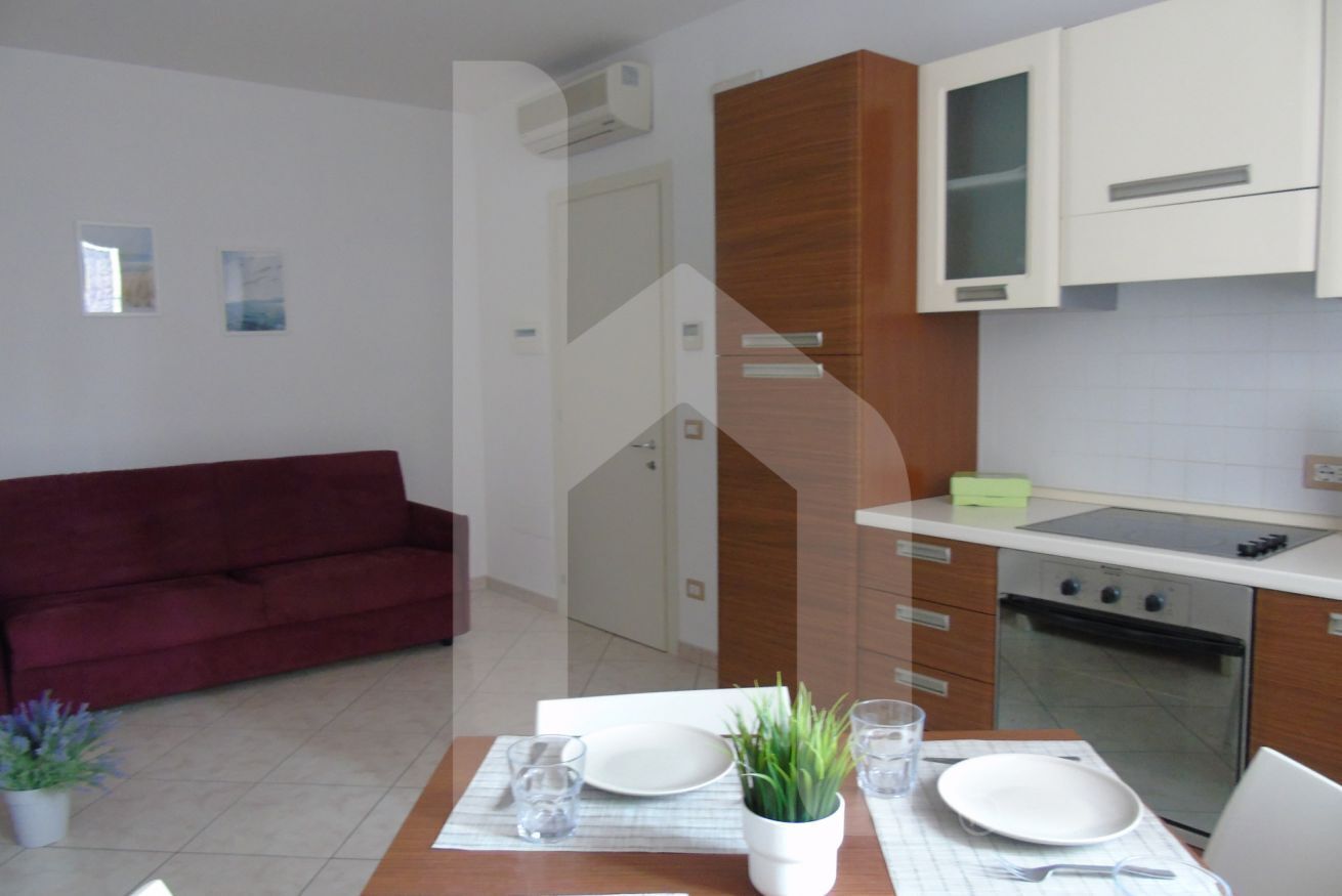 Une cuisine moderne avec des armoires blanches, un four encastré et un coin repas avec une table dressée pour deux personnes.