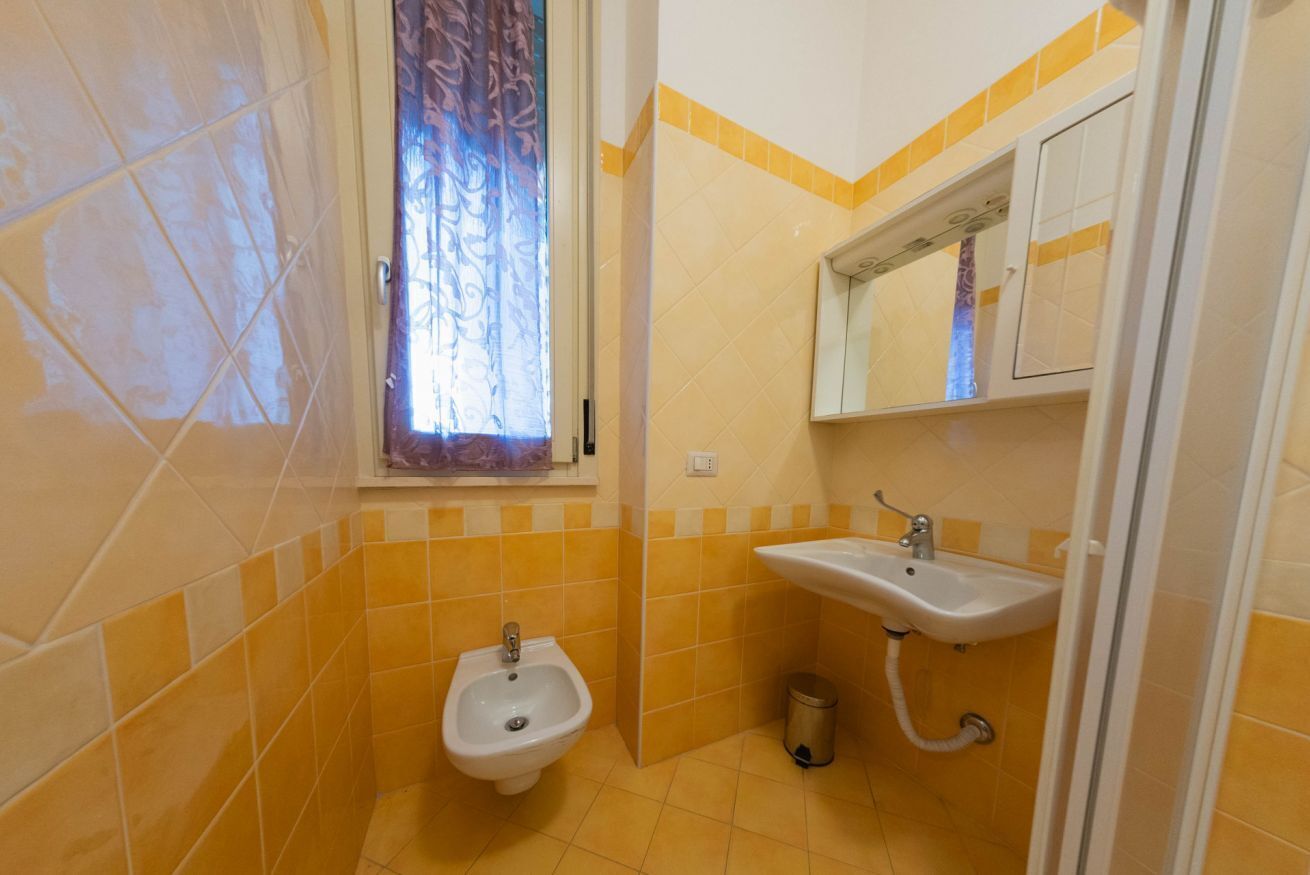 A bathroom with yellow tiles, a bidet, a sink, and a window with a curtain.