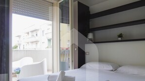A hotel room with a bed, a small table, a chair, and a view of the outside. - Homiday - Felicioni Alba Adriatica, Trilocale al 1°piano (Alba Adriatica)