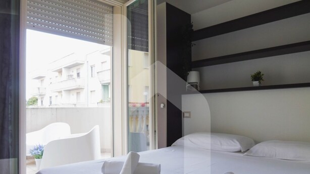 A hotel room with a bed, a small table, a chair, and a view of the outside.