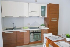 A modern kitchen with white and wooden cabinets, a built-in oven, and a dining area with a table set for two. - Homiday - Felicioni Alba Adriatica, Two-Bedroom Apartment (Alba Adriatica)