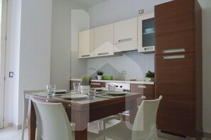A modern kitchen with white cabinets, a wooden dining table, and chairs. - Homiday - Felicioni Alba Adriatica, Two-Bedroom Apartment (Alba Adriatica)