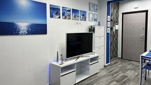 Ein modernes Zimmer mit einem großen Flachbildfernseher auf einer weißen Unterhaltungsanlage, einer Tür mit gemustertem Vorhang und einer blau-weißen Farbgestaltung.