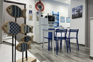 Une cuisine moderne avec un coin repas, comprenant une horloge, un réfrigérateur, un four à micro-ondes et des chaises bleues.