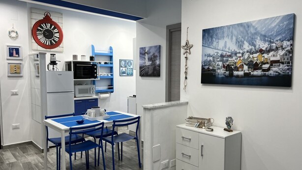 A compact kitchen with a dining area, white cabinetry, and a blue table. - Brand new apartment near the sea (Fuscaldo)