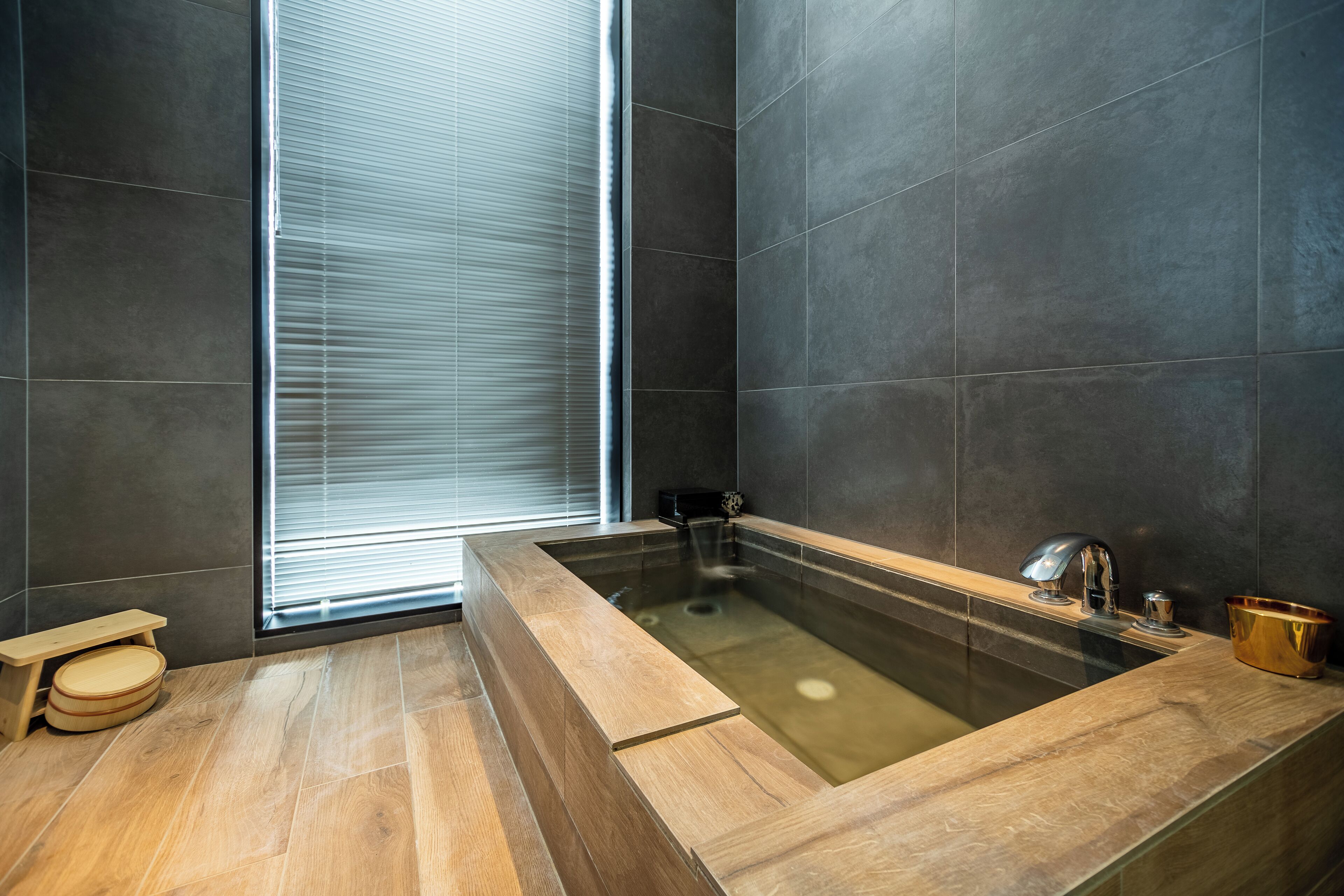 Een moderne badkamer met een groot bad, houten vloeren en donkere tegels.