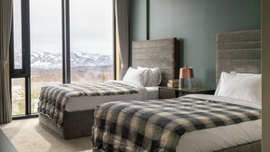 Une chambre d’hôtel avec deux lits, une grande fenêtre donnant sur les montagnes et une table de chevet avec une lampe.