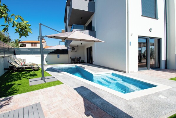 A modern outdoor swimming pool with a covered seating area and lounge chairs.