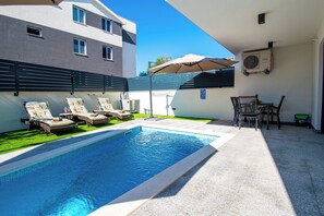A swimming pool with lounge chairs, a table, and chairs.