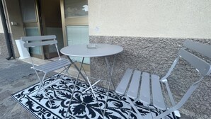 A small outdoor seating area with a table and two chairs, a patterned rug, and a building entrance. - Dante Apartment (Porto Azzurro)