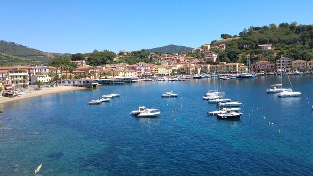 A coastal town with clear blue water, boats, and buildings along the shore. - Dante Apartment (Porto Azzurro)