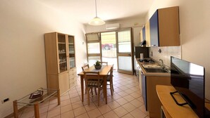A compact kitchen with a dining table, a cabinet, and a small table with a plant. - Dante Apartment (Porto Azzurro)