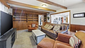 A living room with a television, leather sofa, wooden shelves, and a large mirror. - Experience Wichita living near WSU!  Fire Pit, Pool Table, and Arcade games. (Wichita)