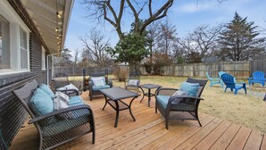 A deck with wicker furniture and a wooden table. - Experience Wichita living near WSU!  Fire Pit, Pool Table, and Arcade games. (Wichita)