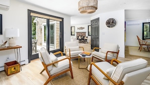 A modern living room with white leather sofas, a wooden coffee table, and a large window with a view of the outdoors.