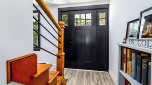 A black door with a window, a wooden staircase, and a bookshelf with books.