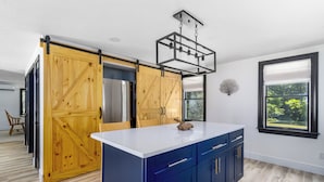 A modern kitchen with a large island, blue cabinets, and a wooden barn-style door.