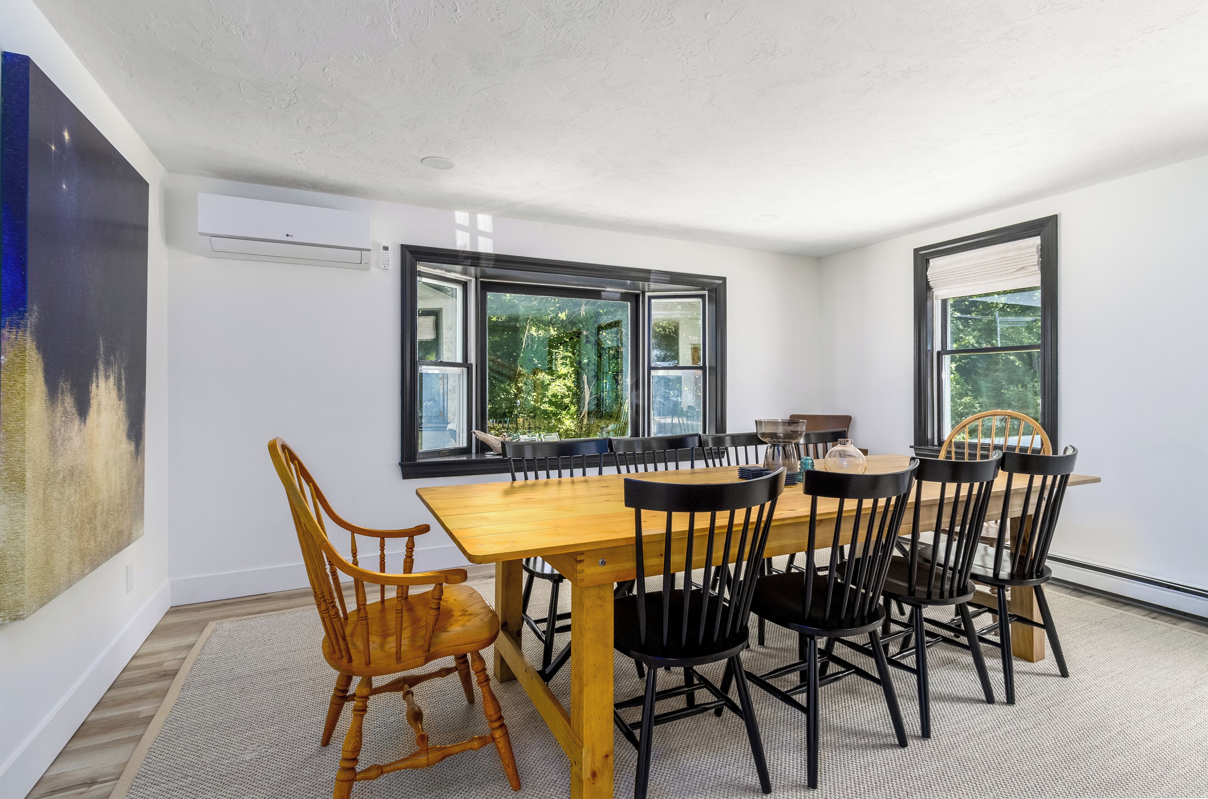 A dining area with a wooden table and chairs, large windows, and an air conditioning unit.