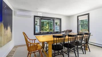 A dining area with a wooden table and chairs, large windows, and an air conditioning unit.