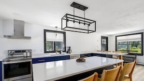 A modern kitchen with a central island, stainless steel appliances, and a large window providing a view of the outdoors.