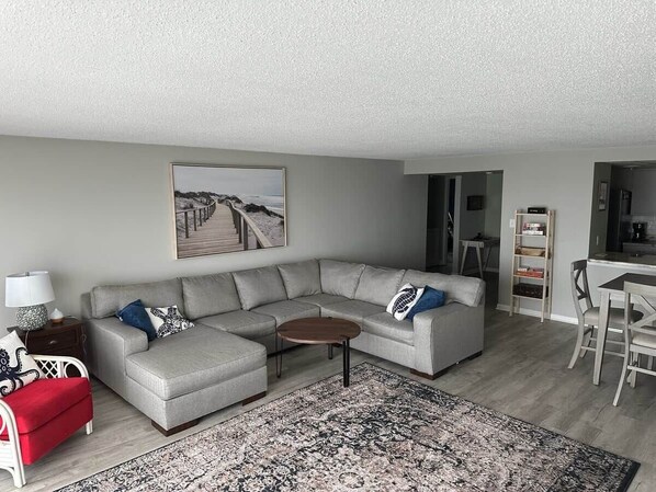 A living room with a sectional sofa, a coffee table, a red chair, a rug, and a painting on the wall.
