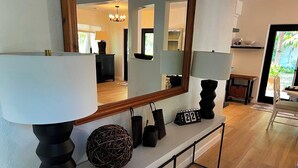 A modern living room with a large mirror, a white console table, and a black clock displaying the date.