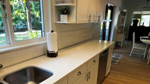 A kitchen with white cabinets, a stainless steel sink, a dishwash, and a window with a view of greenery.