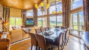 Un vaste espace dédié à la salle à manger, avec une longue table et de nombreuses chaises, de grandes fenêtres offrant une vue panoramique et un téléviseur fixé au mur.