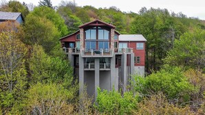 Une maison à deux étages avec un balcon au niveau supérieur, entourée d’une végétation luxuriante.