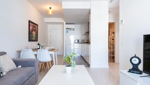 A modern living room with a sofa, a dining table, and a coffee table. There is a kitchen in the background with white cabinets and a microwave. - MalagaSuite Quintana Holidays (Torremolinos)