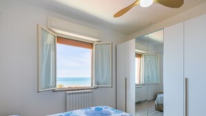 Ein Schlafzimmer mit Bett, einem Fenster mit Meerblick, einem Deckenventilator und einem Kleiderschrank.