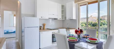 A modern kitchen with white cabinetry, a built-in oven, and a dining area with a table set for two.
