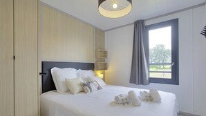 A neatly made bed with white linens and pillows, a bedside lamp, and towels on the bed.