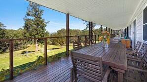 Una terraza de madera con una mesa y sillas, con vistas a un área verde con árboles.
