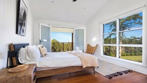 Un dormitorio con una cama grande, cabecera de madera y vistas a los árboles a través de amplias ventanas.
