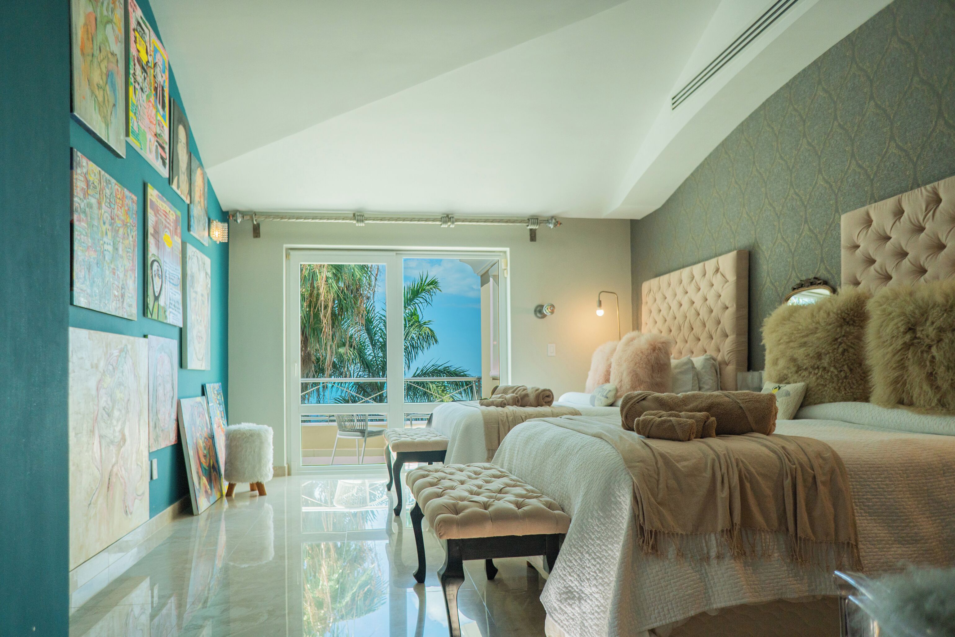 Une chambre spacieuse avec un grand lit, une tête de lit capitonnée et une vue sur les palmiers, visible à travers une porte vitrée.