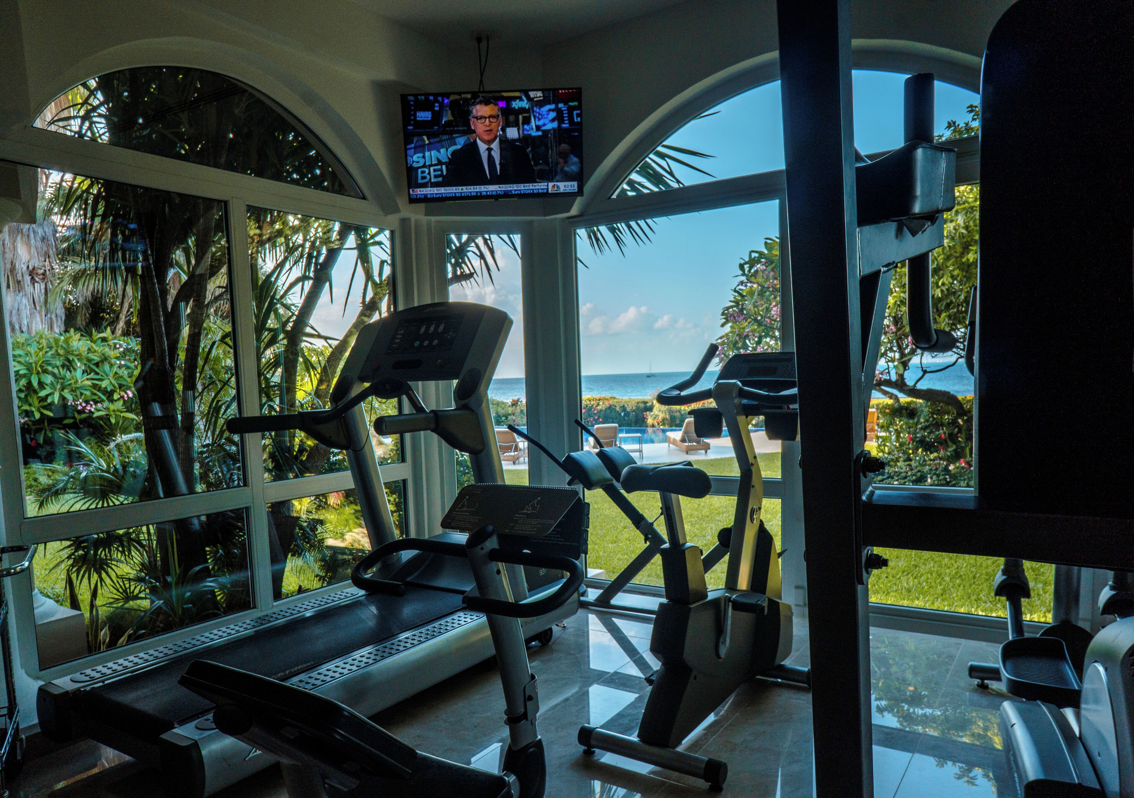 Un gimnasio con equipo de ejercicio y una pantalla de televisión mostrando un noticiero.