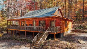 A rustic cabin with a wooden deck, a staircase leading to the entrance, and a forest backdrop. - Saluda Summit at Saluda Grade Cabins! (Saluda)