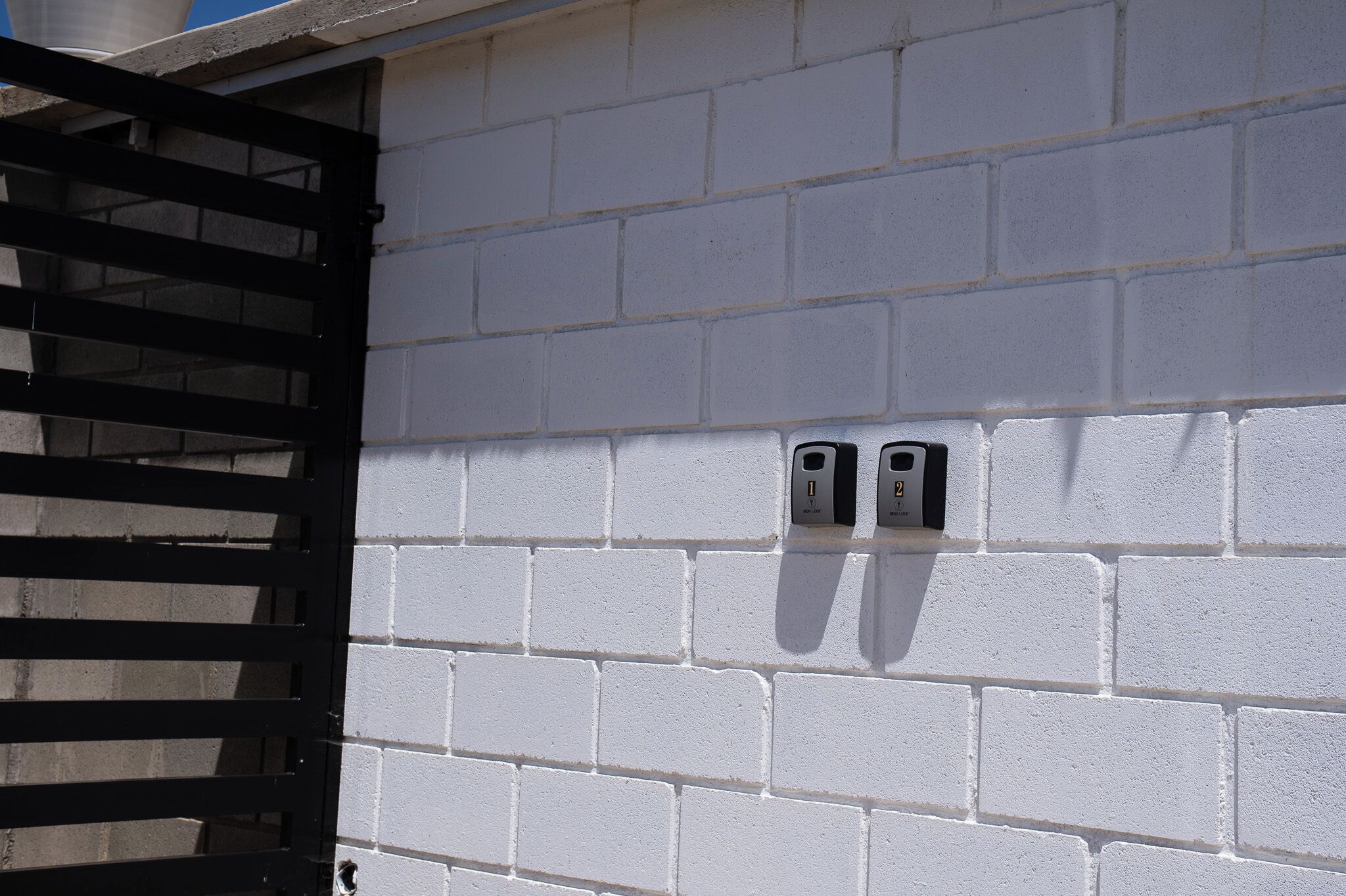 A white brick wall with two electrical outlets and a black metal gate.