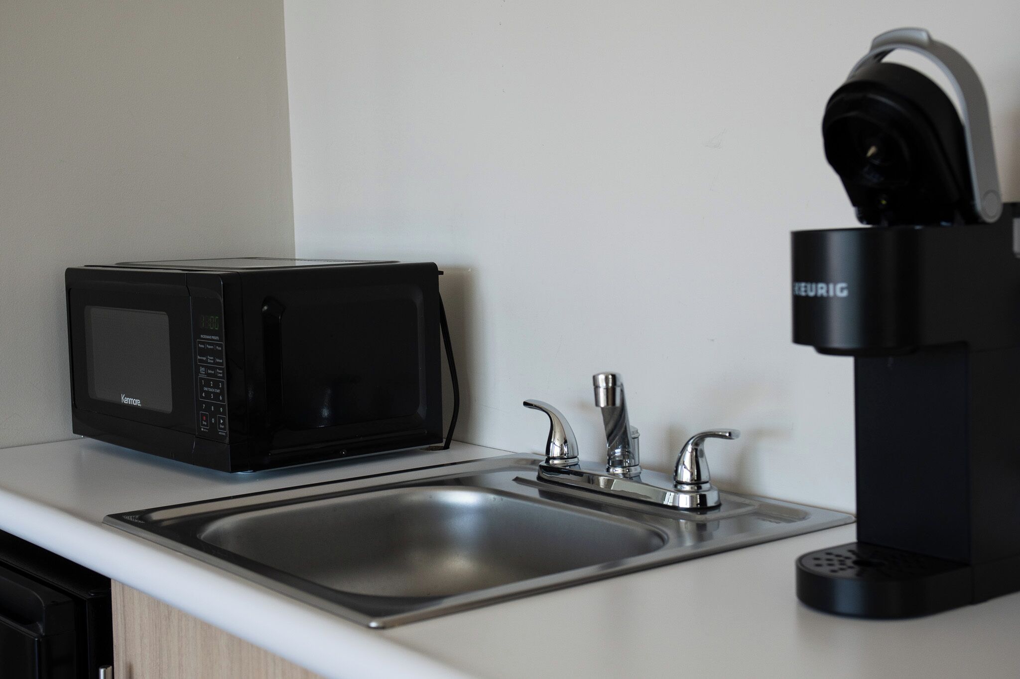 A kitchen with a black microwave, a sink with two faucets, and a black coffee maker.