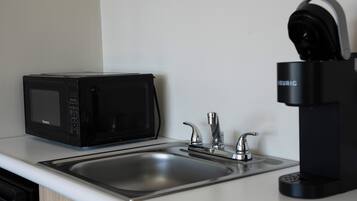 A kitchen with a black microwave, a sink with two faucets, and a black coffee maker.