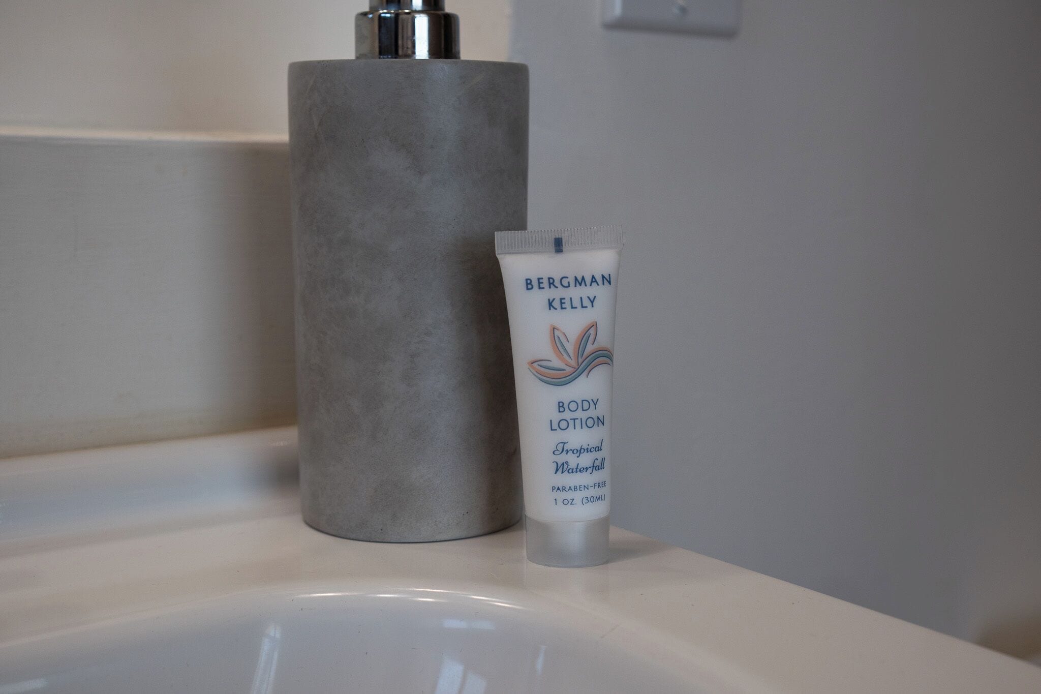 Un lavabo de salle de bain avec un tube de lotion pour le corps de la marque Bergman Kelly et un récipient cylindrique.