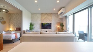 A modern hotel room with a large bed, a sofa, a TV mounted on the wall, and a balcony with a chair.
