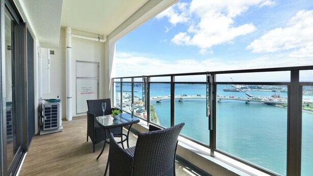 A balcony with a table and chairs, overlooking a marina with boats and a bridge.